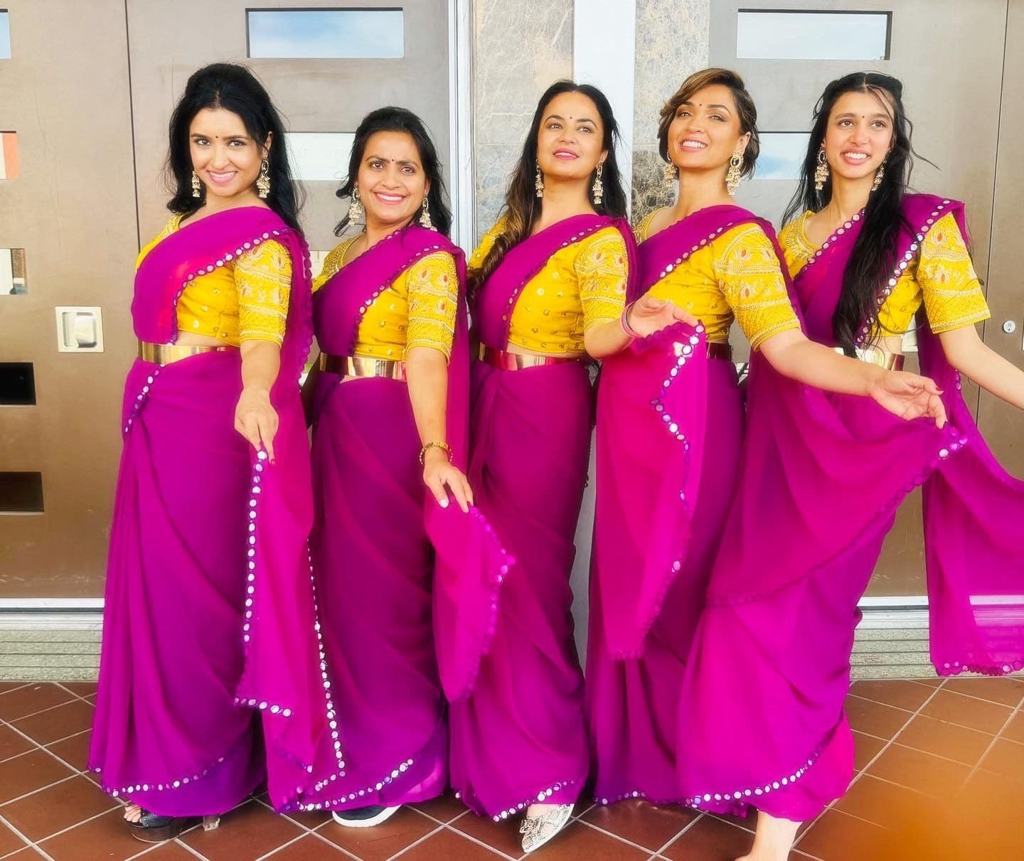Five women in matching magenta and gold sarees